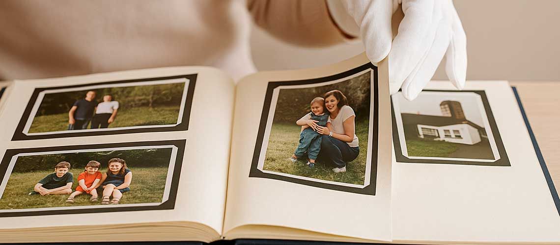 Person wearing white cotton gloves turning pages of a family photo album.
